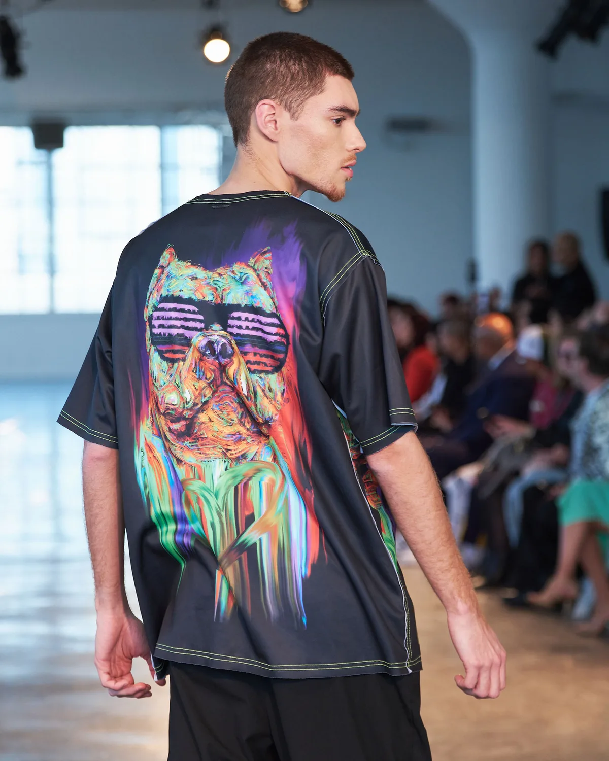 Model in a black tee printed with a psychedelic cat in sunglasses, walking the FDLA runway