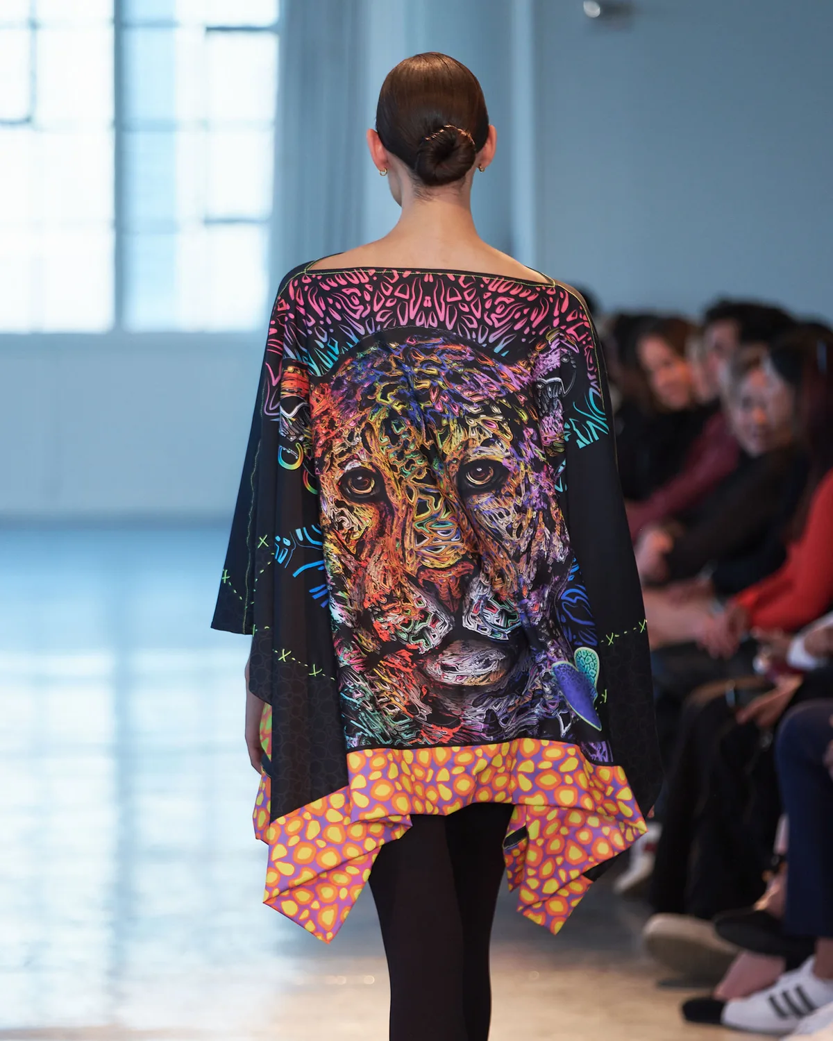 Model in a flowing black poncho carrying a full-back leopard portrait in engraved colour linework