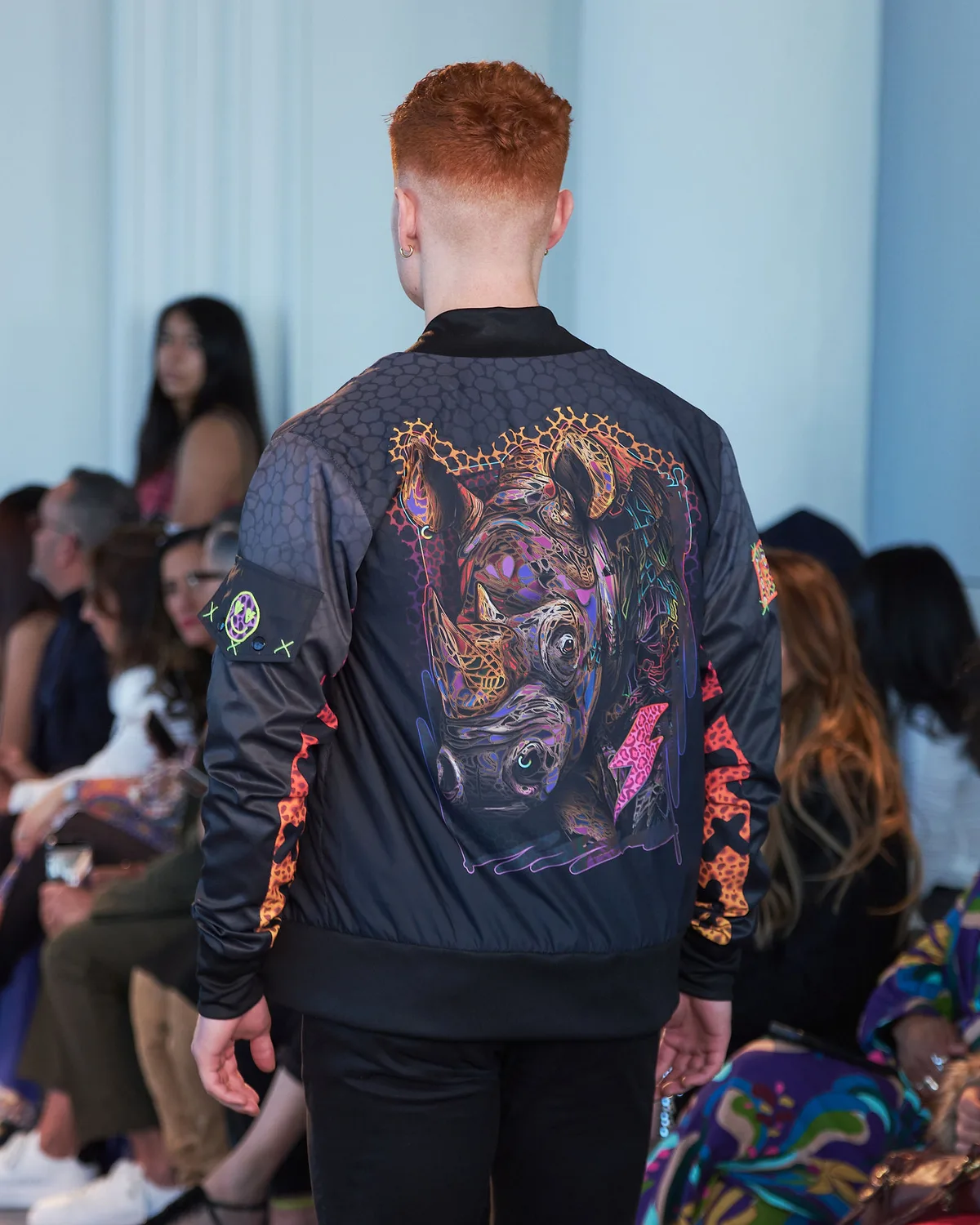 Model in a black bomber jacket printed with a rhinoceros and companion characters in neon engraved lines